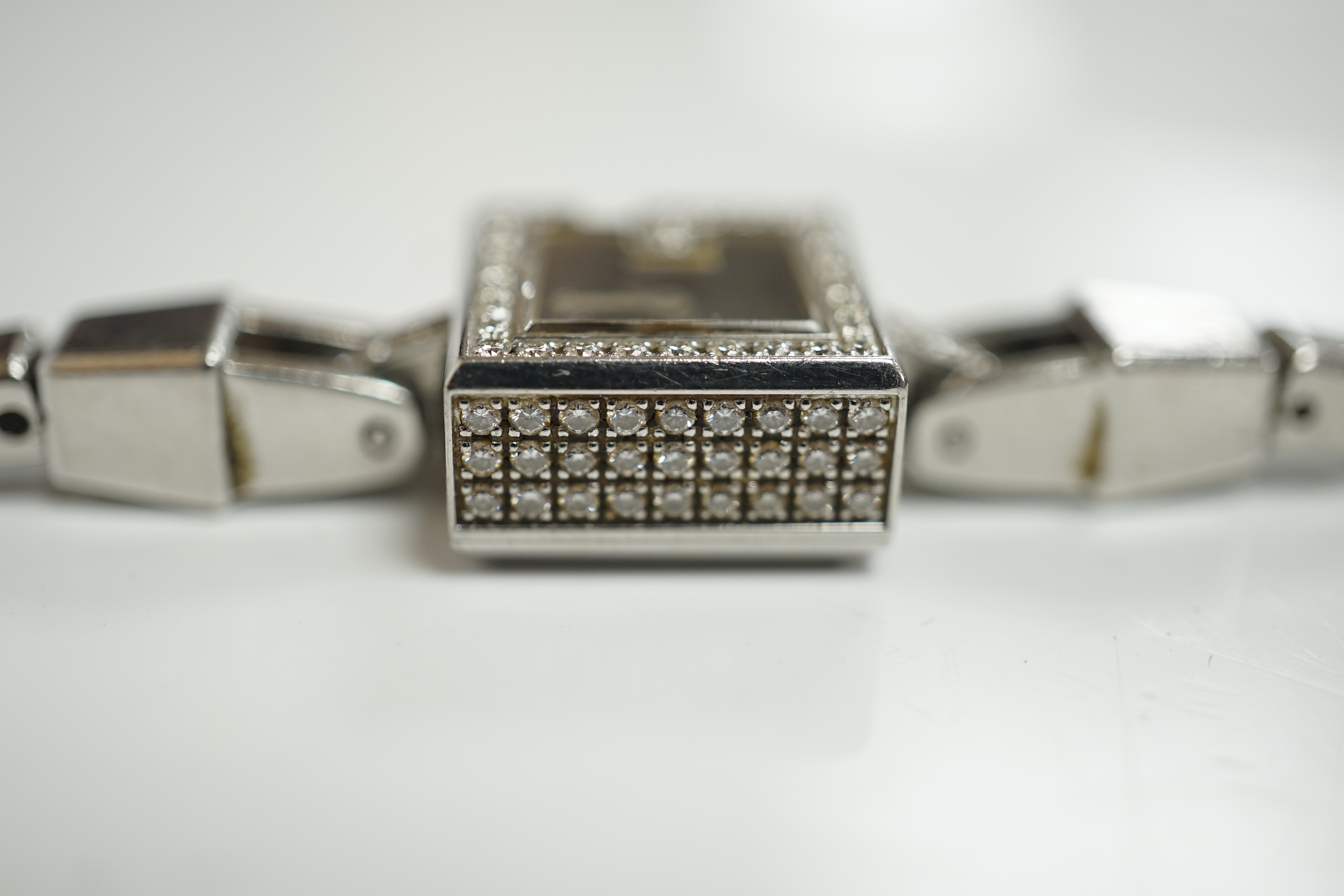 A lady's stainless steel Gucci quartz wrist watch, with G shaped case and diamond chip set bezel, on a stainless steel Gucci bracelet. Condition - fair